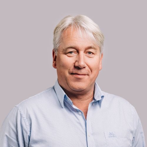 En middelaldrende mann med kort, grått hår og lyseblå skjorte står mot en ensfarget, lysegrå bakgrunn.